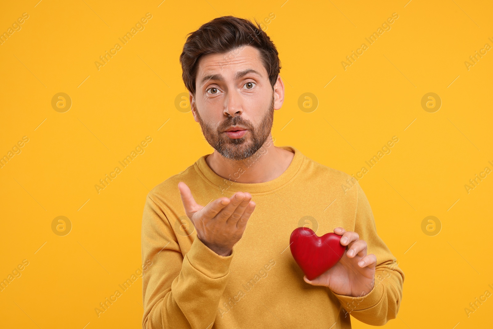 Photo of Man holding red heart and blowing kiss on orange background