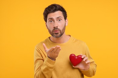 Man holding red heart and blowing kiss on orange background