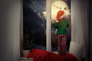 Image of Cute little girl on window sill at home waiting for Santa Claus. Christmas celebration
