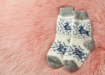 Photo of Knitted socks on pink faux fur, flat lay. Space for text