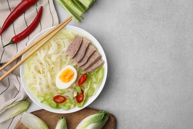Bowl of delicious rice noodle soup with meat and egg on light grey table, flat lay. Space for text
