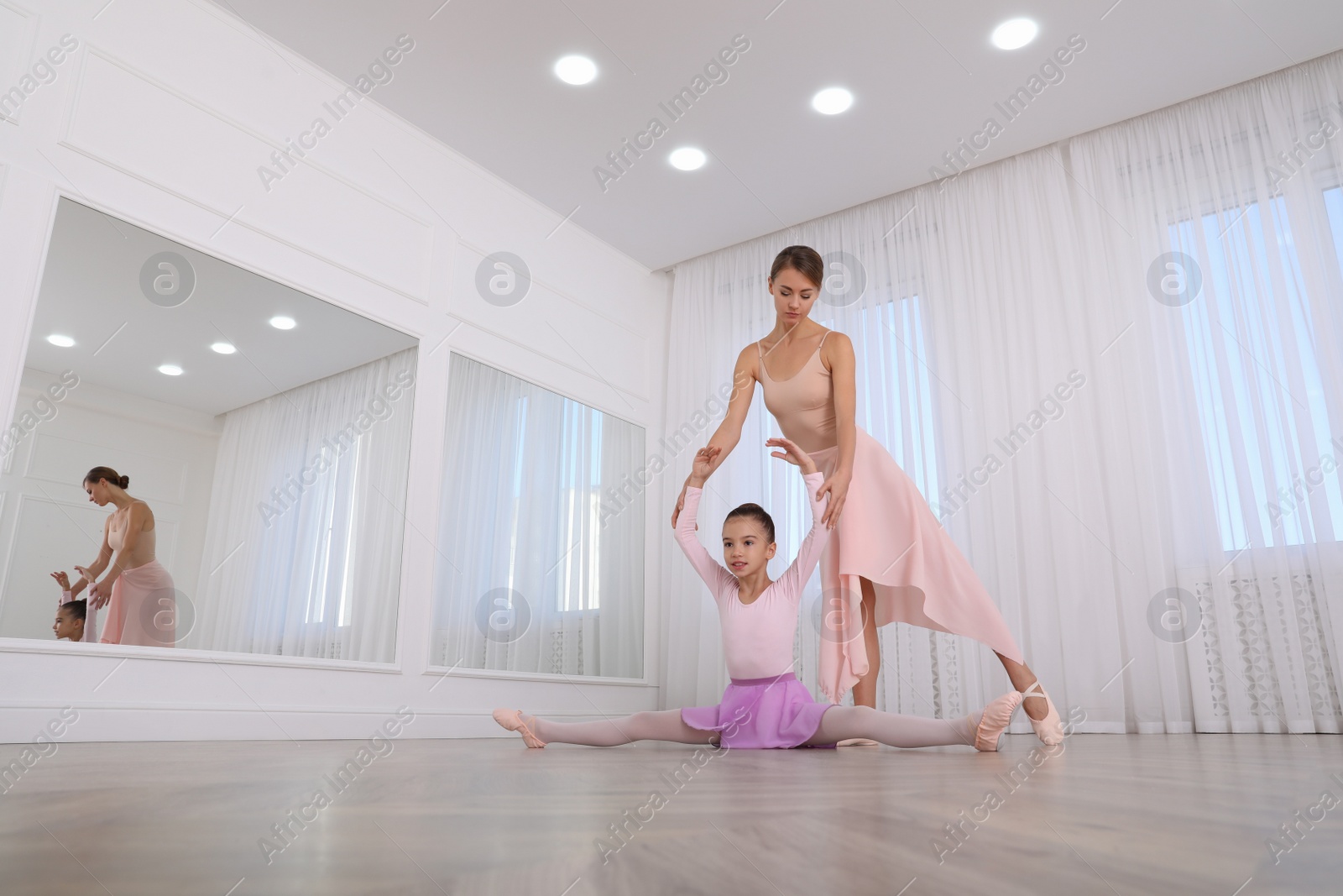 Photo of Ballet teacher helping little girl to stretch on floor in dance studio