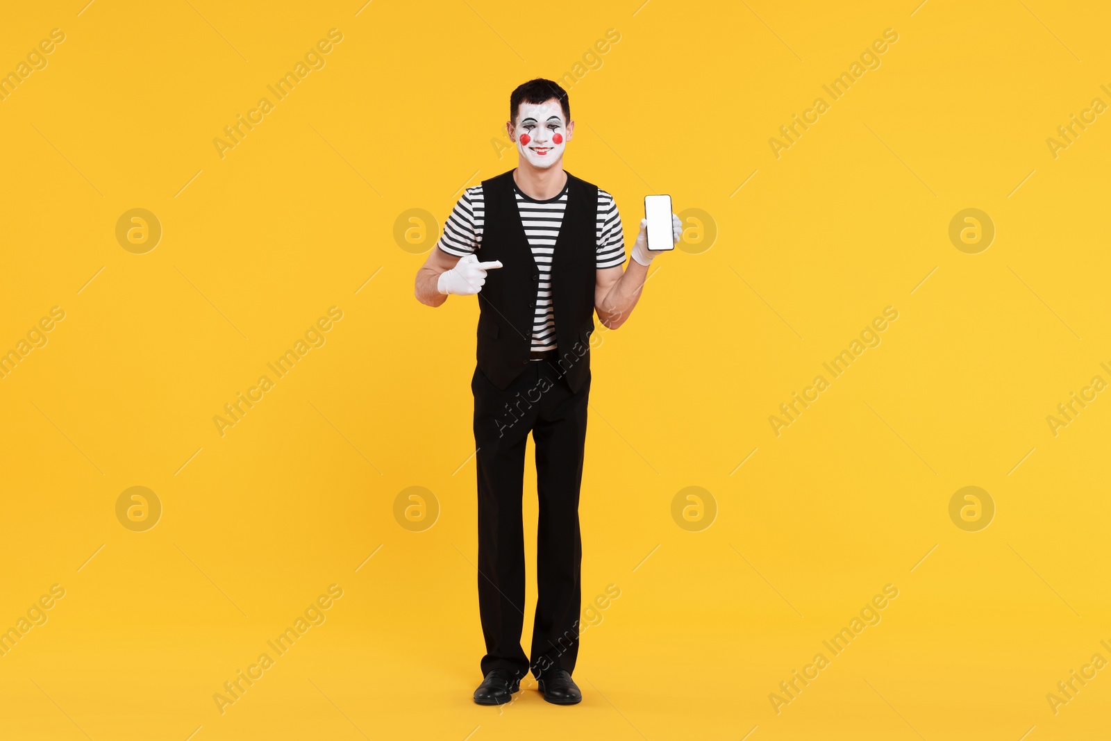 Photo of Funny mime artist pointing at smartphone on orange background