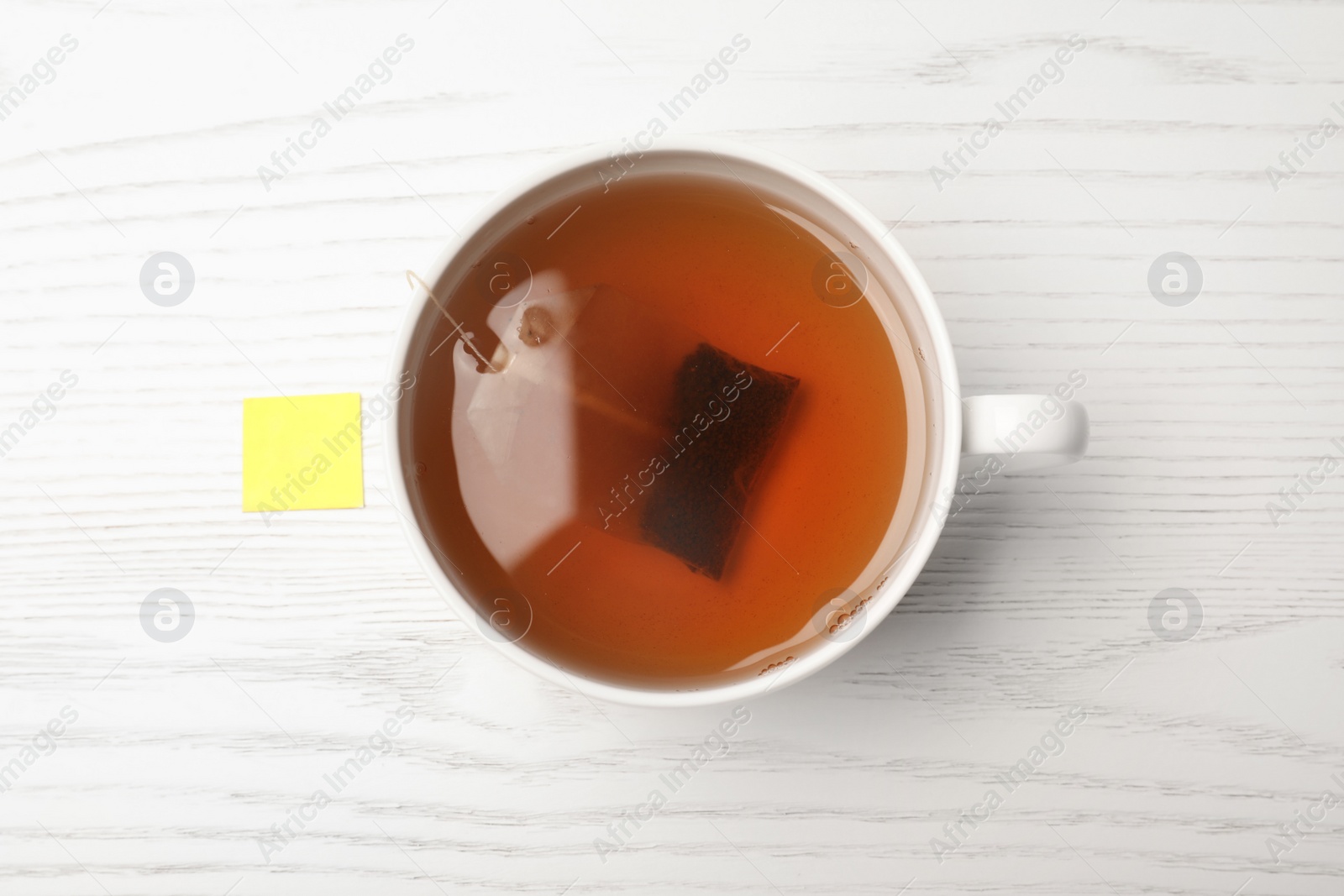 Photo of Cup of hot fresh tea with bag on wooden background, top view