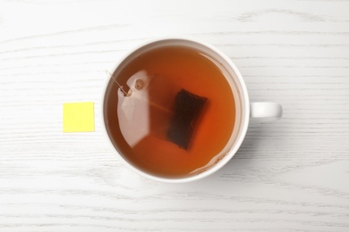 Photo of Cup of hot fresh tea with bag on wooden background, top view