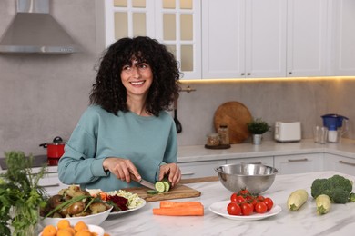 Photo of Woman cooking healthy vegetarian meal at white marble table in kitchen