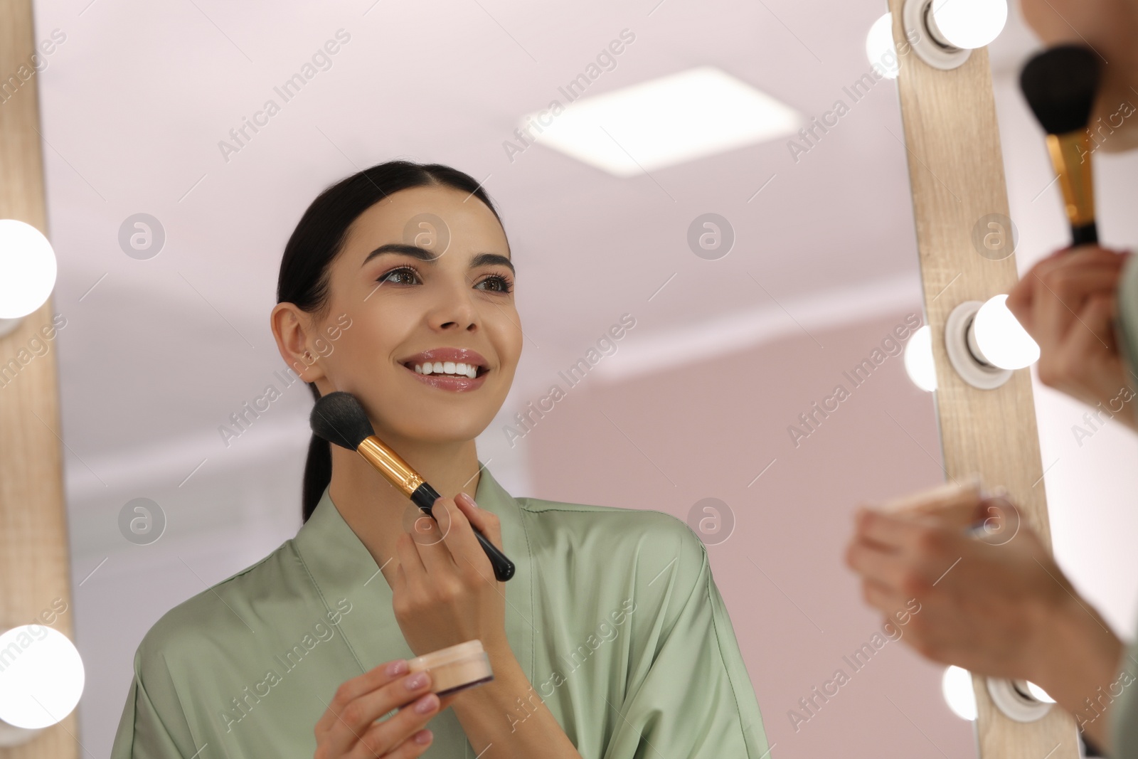 Photo of Reflection of beautiful young woman applying face powder with brush near mirror at home