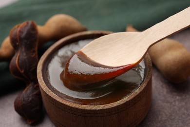 Photo of Taking tasty tamarind sauce with spoon from bowl on brown table, closeup