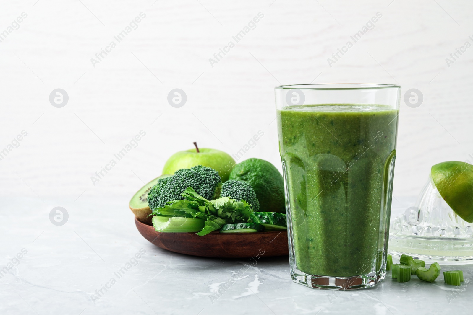 Photo of Delicious green juice and fresh ingredients on grey marble table. Space for text