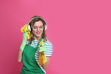 Photo of Beautiful young woman with headphones, rag and bottle of detergent singing on pink background. Space for text