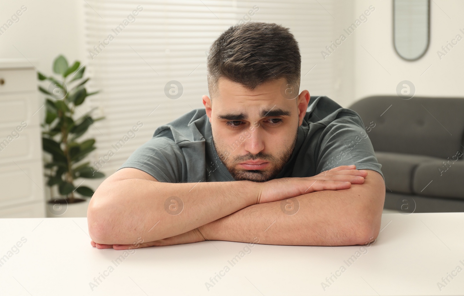 Photo of Sad man sitting at white table indoors