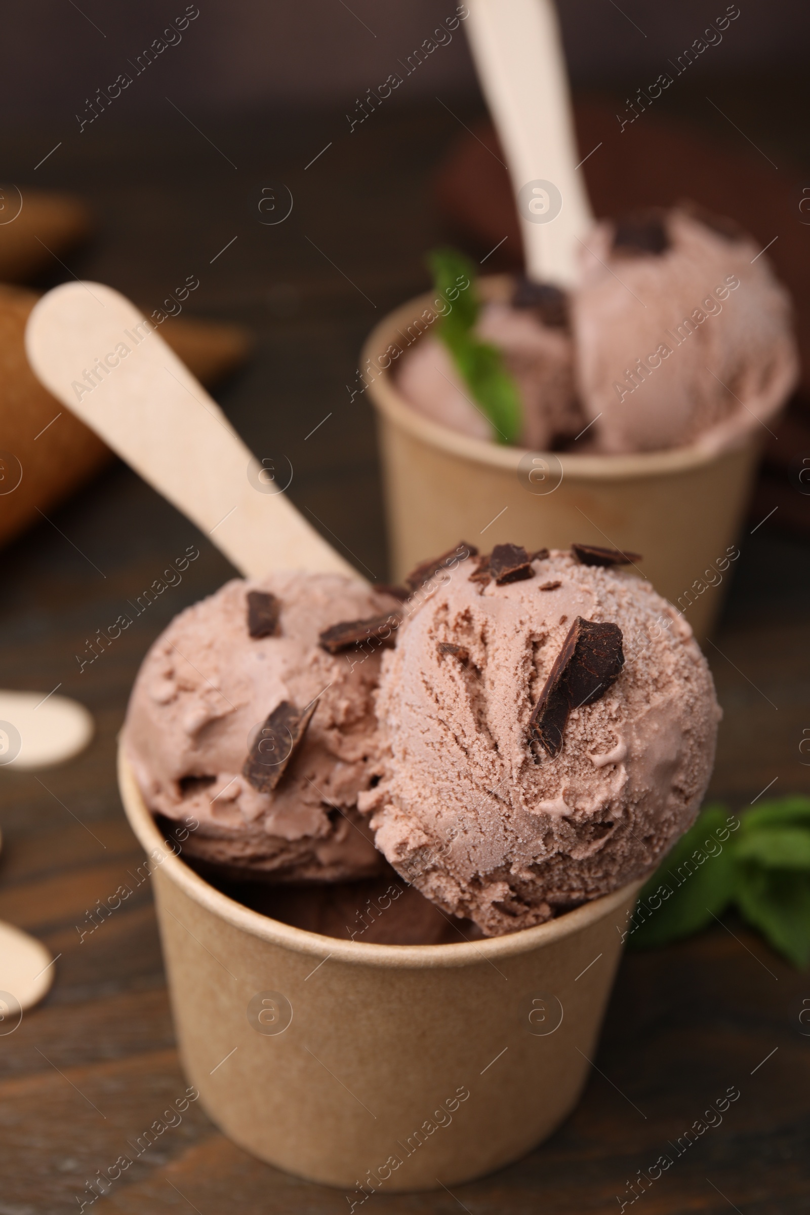 Photo of Paper cups with tasty chocolate ice cream on wooden table, closeup