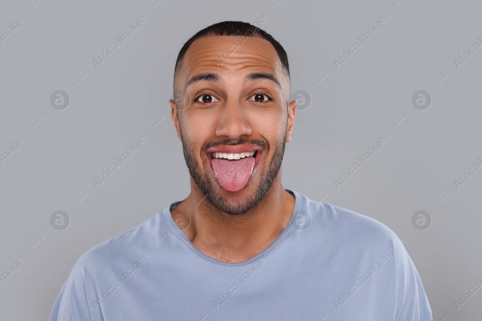 Photo of Happy young man showing his tongue on light grey background