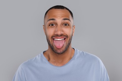 Happy young man showing his tongue on light grey background