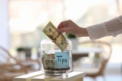 Photo of Woman putting tips into glass jar at table, closeup