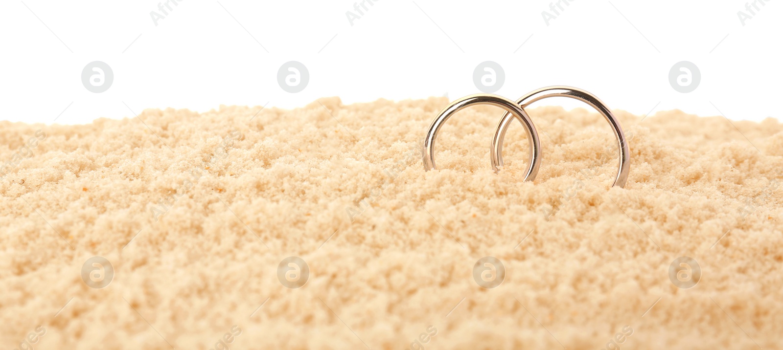 Photo of Honeymoon concept. Two golden rings and sand isolated on white