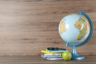 Photo of Globe, books, magnifying glass and apple on wooden table, space for text. Geography lesson