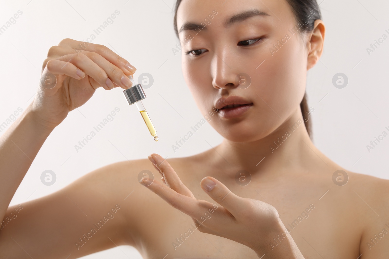 Photo of Beautiful young woman applying cosmetic serum onto her finger on white background, selective focus