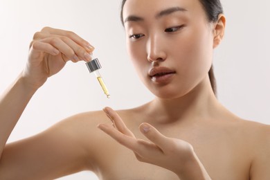 Photo of Beautiful young woman applying cosmetic serum onto her finger on white background, selective focus