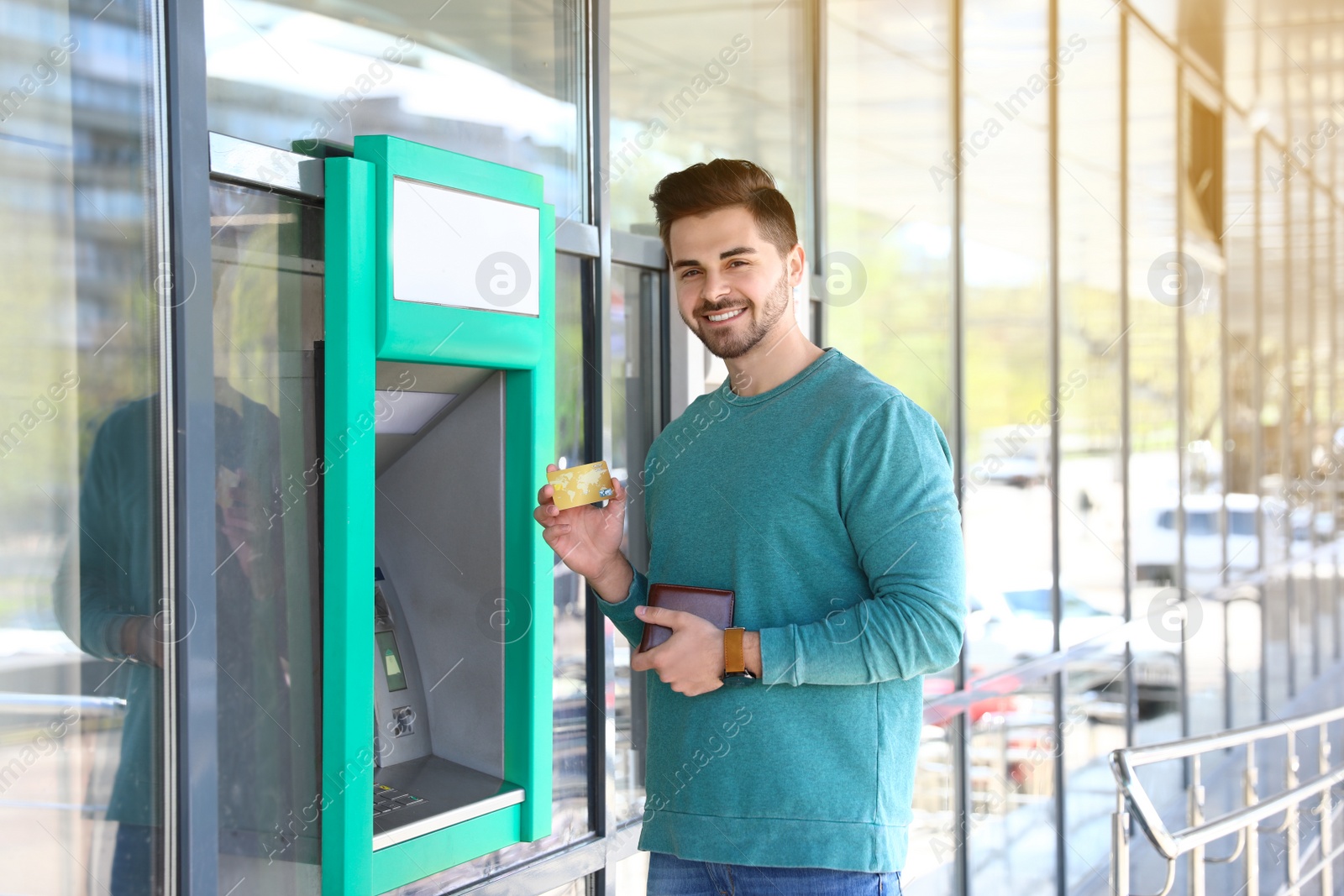 Photo of Young man with credit card near cash machine outdoors