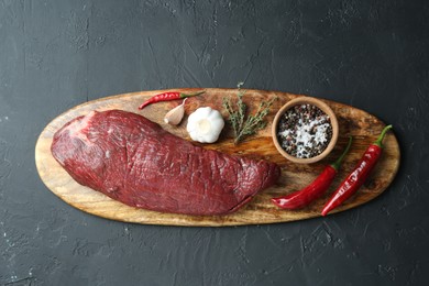 Photo of Piece of raw beef meat, products and spices on dark textured table, top view