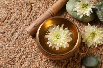 Photo of Tibetan singing bowl with water, beautiful chrysanthemum flowers, mallet and stones on table, above view. Space for text
