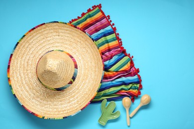Photo of Mexican sombrero hat, maracas, toy cactus and colorful poncho on light blue background, flat lay. Space for text