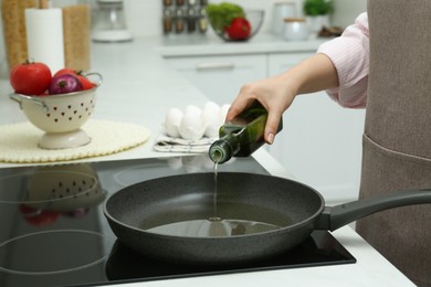 Woman pouring oil from jug into pan in kitchen, closeup