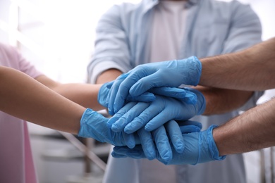 Group of people in blue medical gloves stacking hands indoors, closeup