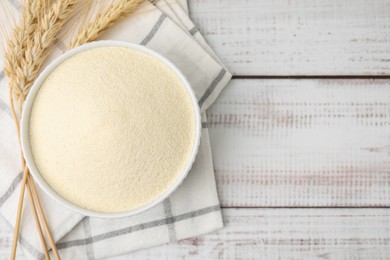 Uncooked organic semolina in bowl and spikelets on white wooden table, top view. Space for text