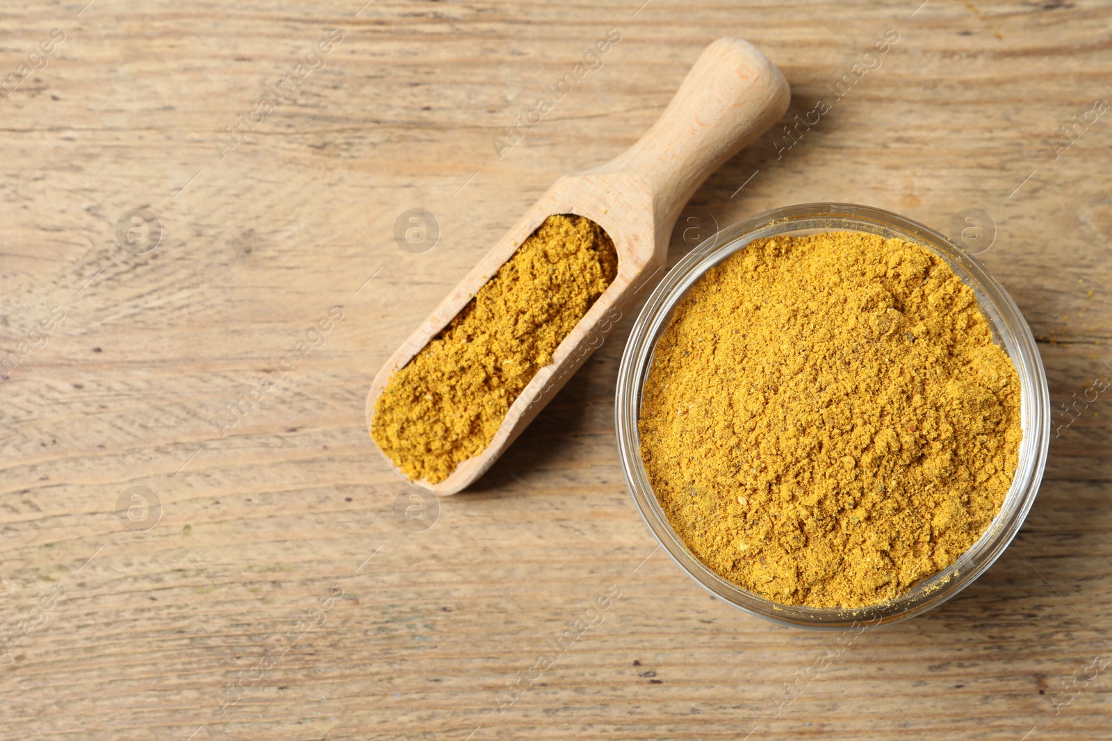 Photo of Curry powder in bowl and scoop on wooden table, top view. Space for text