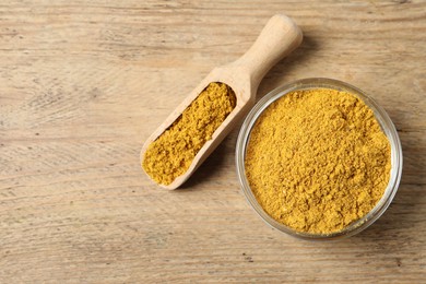 Curry powder in bowl and scoop on wooden table, top view. Space for text