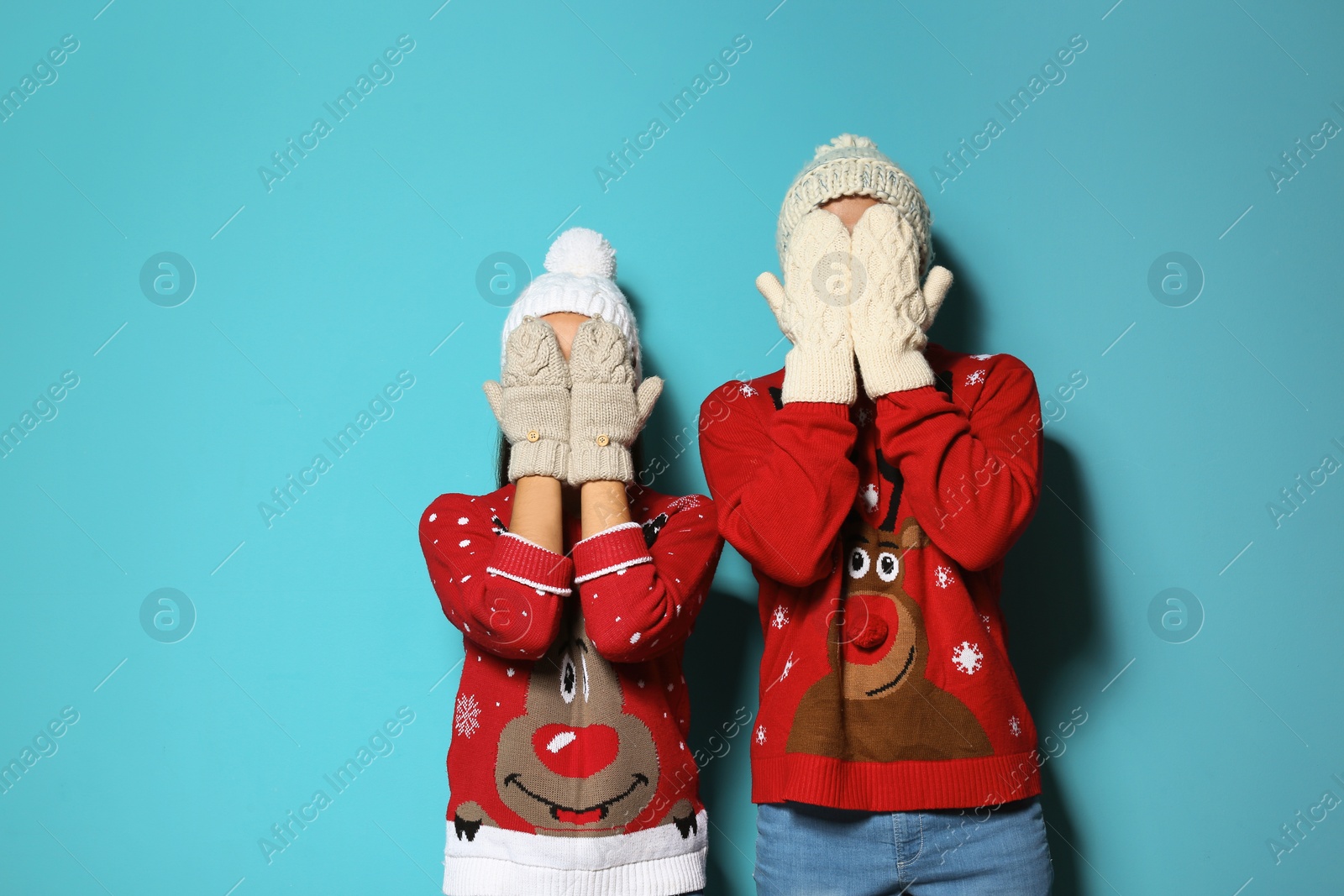 Photo of Young couple in Christmas sweaters and knitted hats on color background