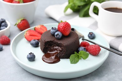 Plate with delicious chocolate fondant, berries and mint on grey table, closeup