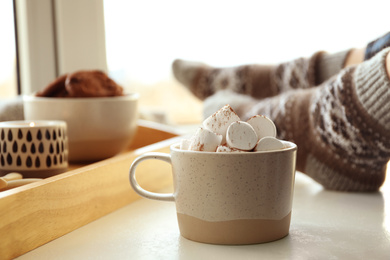 Cup of delicious hot cocoa with marshmallows near window indoors. Winter drink