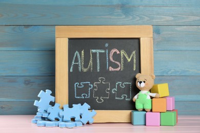 Photo of Small blackboard with word Autism and toys on pink wooden table