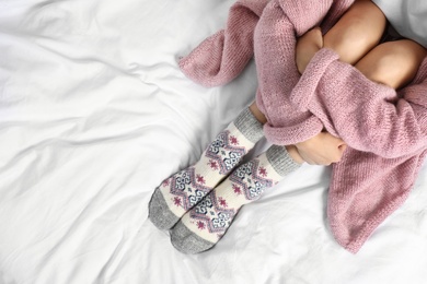 Woman wearing knitted socks on white fabric, top view with space for text. Warm clothes