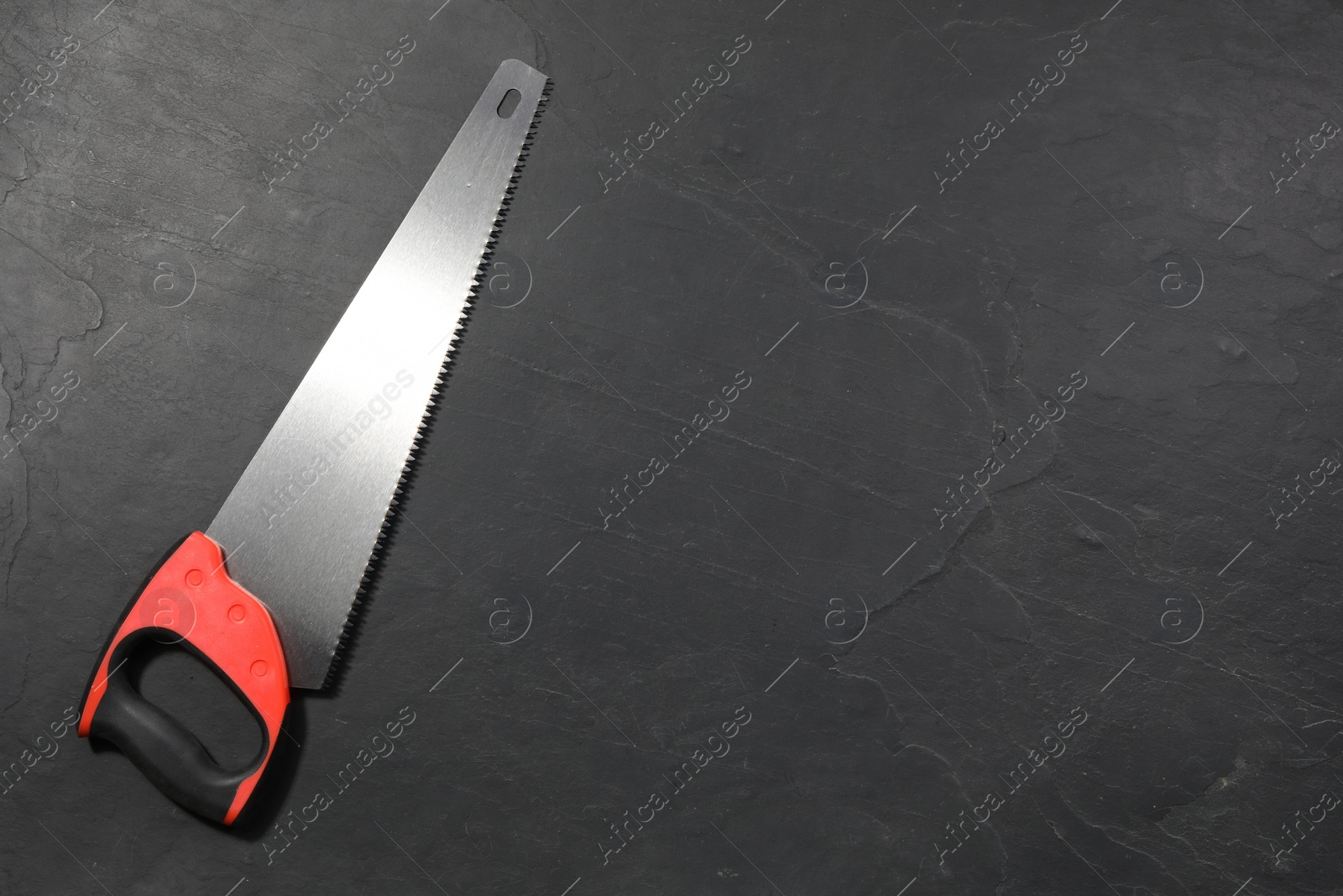 Photo of Saw with colorful handle on black textured background, top view. Space for text
