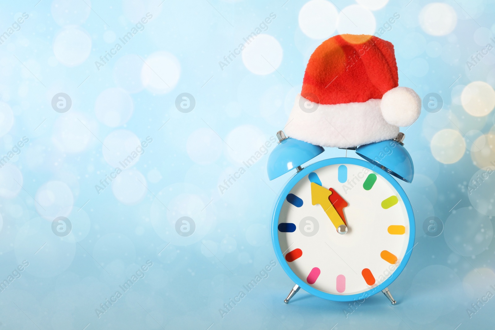 Photo of Alarm clock with Christmas decor on light blue background, space for text. New Year countdown