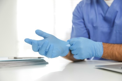 Doctor putting on medical gloves at table in office, closeup