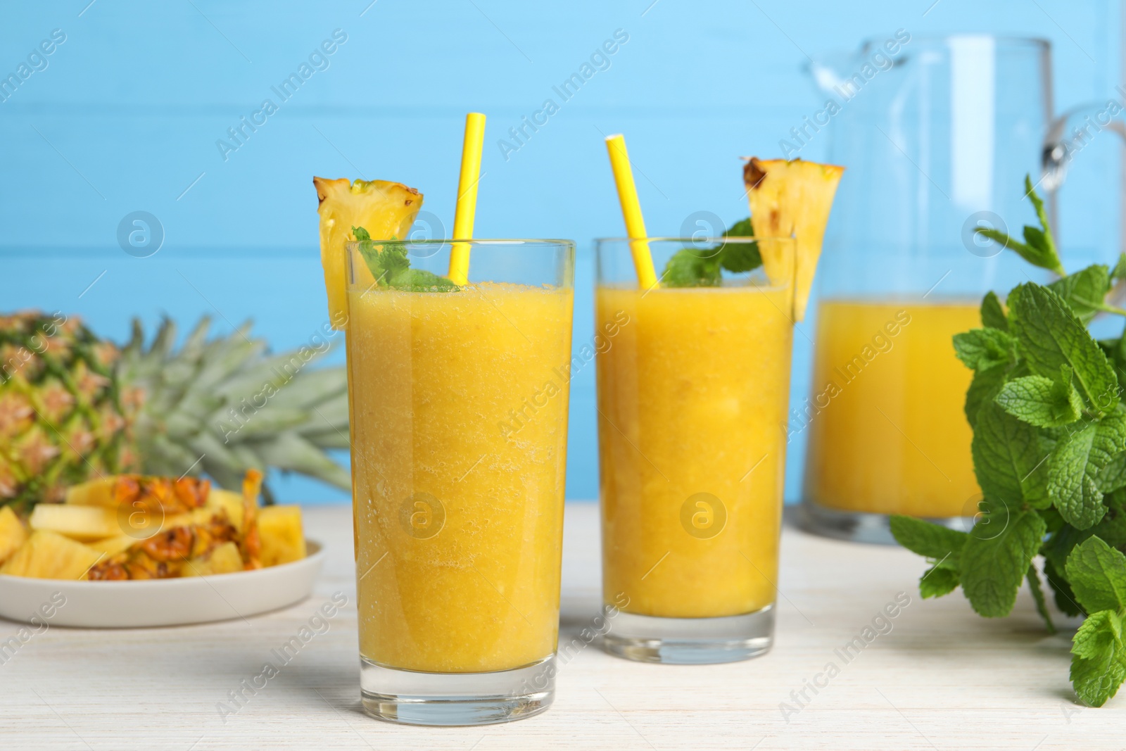 Photo of Tasty pineapple smoothie, mint, cut and whole fruits on white wooden table