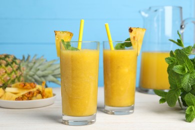 Tasty pineapple smoothie, mint, cut and whole fruits on white wooden table