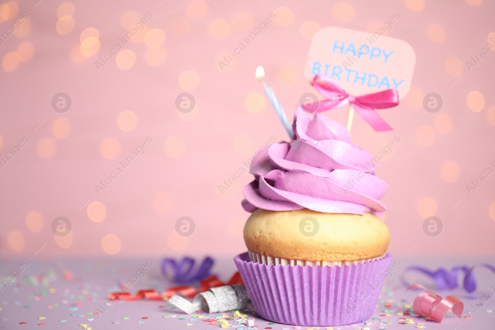 Photo of Beautiful birthday cupcake, streamers and confetti against pink background with blurred lights