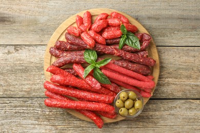 Photo of Different thin dry smoked sausages, basil and olives on wooden table, top view