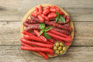 Different thin dry smoked sausages, basil and olives on wooden table, top view