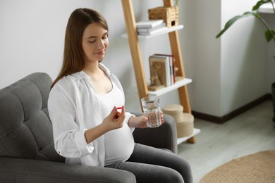 Beautiful pregnant woman holding pill and glass with water at home