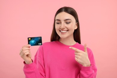 Photo of Happy woman pointing at credit card on pink background