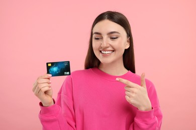 Happy woman pointing at credit card on pink background