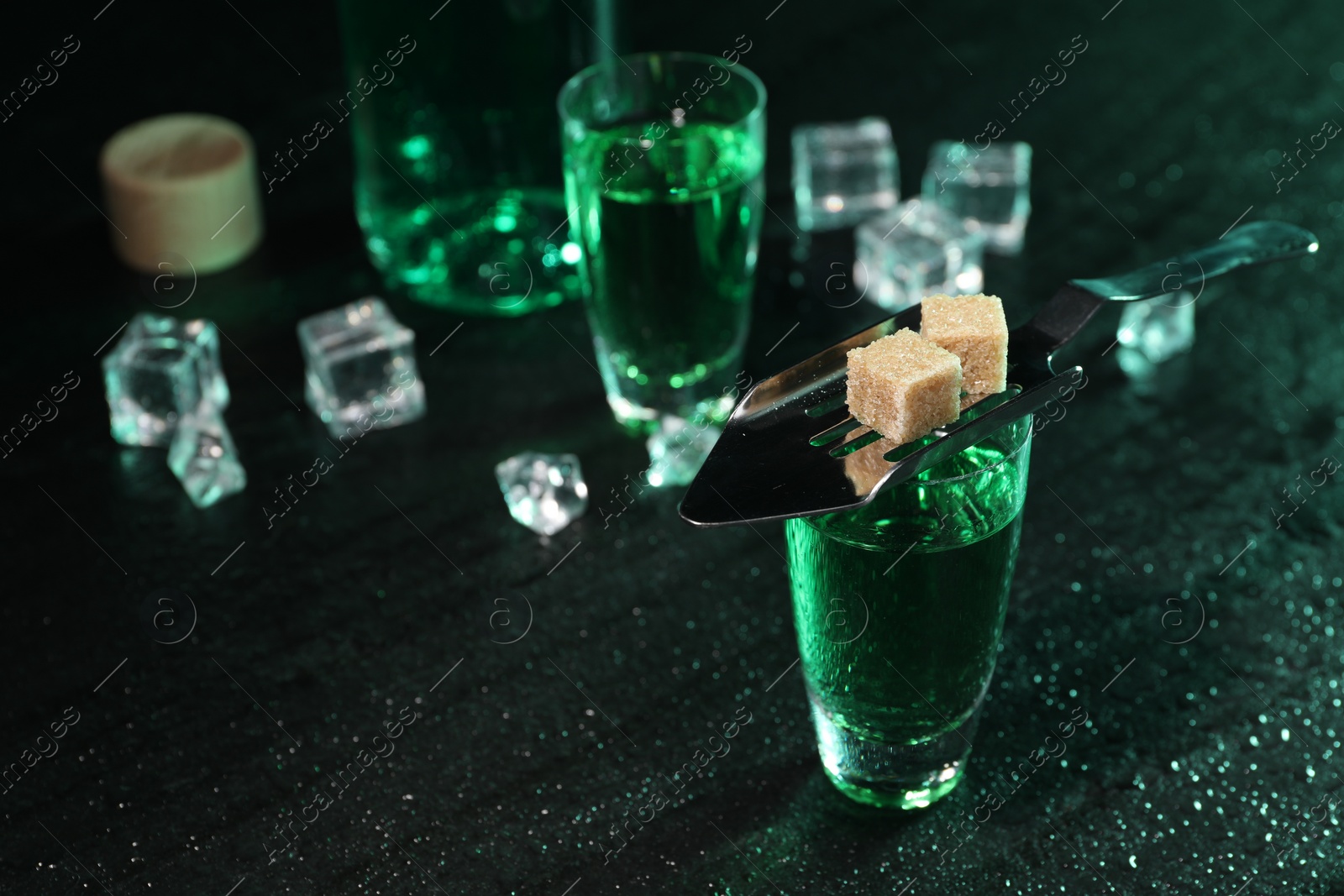 Photo of Absinthe in shot glasses, spoon, brown sugar and ice cubes on gray table, closeup. Alcoholic drink