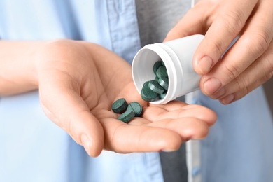 Photo of Woman pouring spirulina pills from bottle into hand, closeup